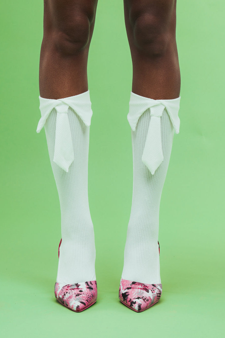 White knee-high socks with ruffles and pink floral shoes on a green background