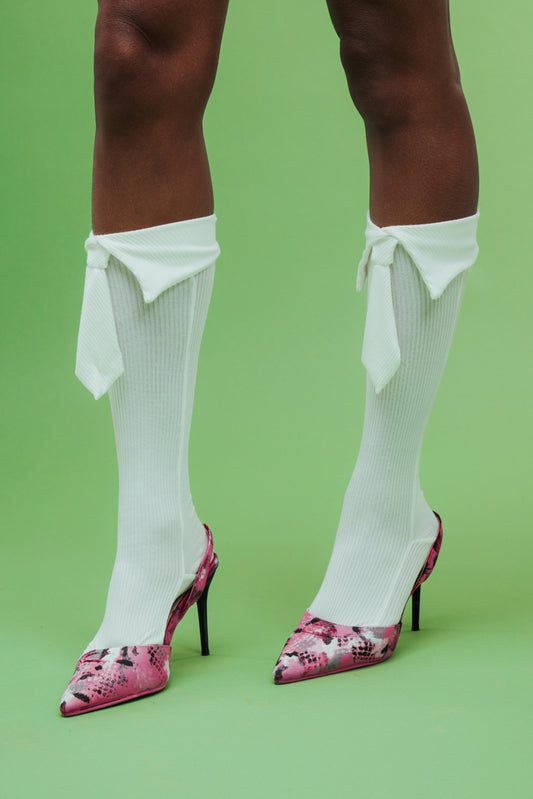 White knee-high socks with ruffles and pink high-heeled shoes on a green background