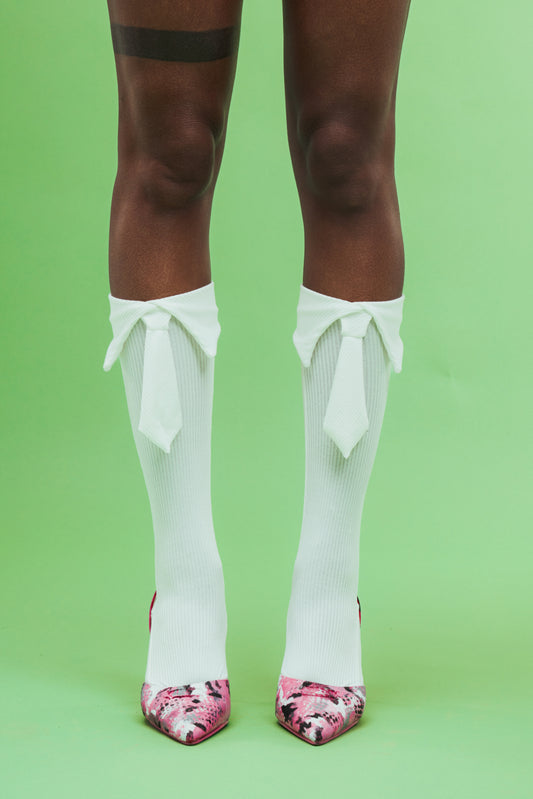 White knee-high socks with ruffles and pink floral shoes on a green background